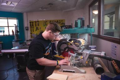 在工程和物理系的实验室里，24岁的杰里米·奥尔盖耶(Jeremey Allgeyer)用圆锯修剪一块木头.